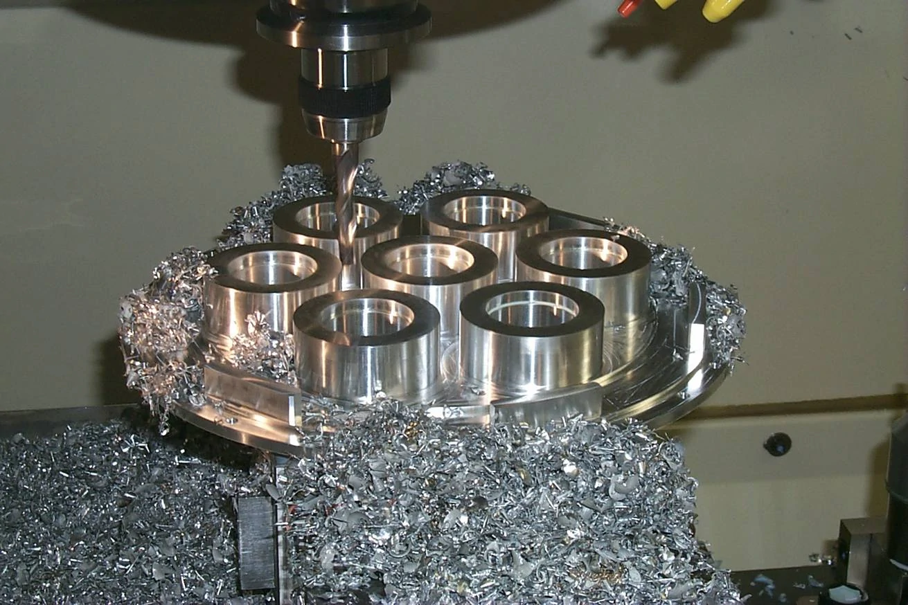 Precision grinding of metal castings using a CNC machine to improve surface finish and dimensional accuracy, with shavings visible around the components.