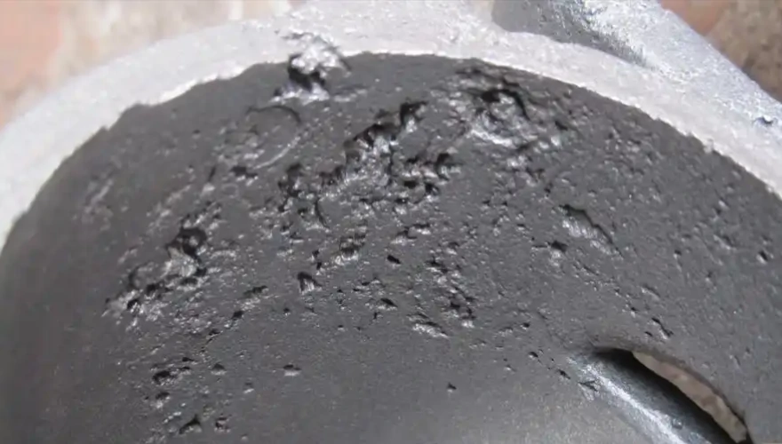 لقطة مقربة لجزء معدني مصبوب تظهر عيوب الانكماش والمسامية، مما يوضح مشاكل جودة الصب الشائعة في المسابك.