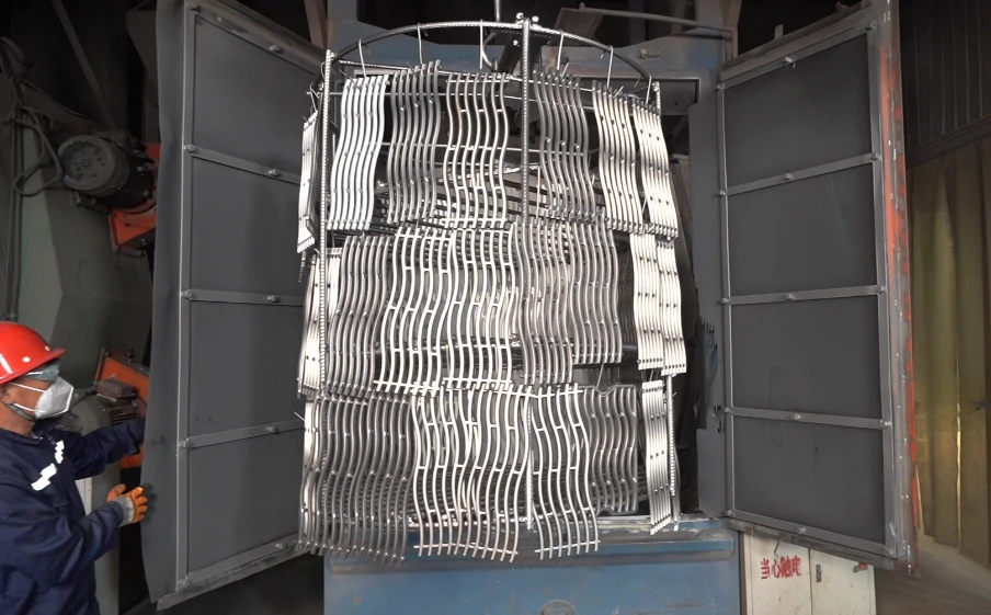 Operator opening shot blasting machine loaded with metal castings for surface cleaning and strengthening in industrial production.