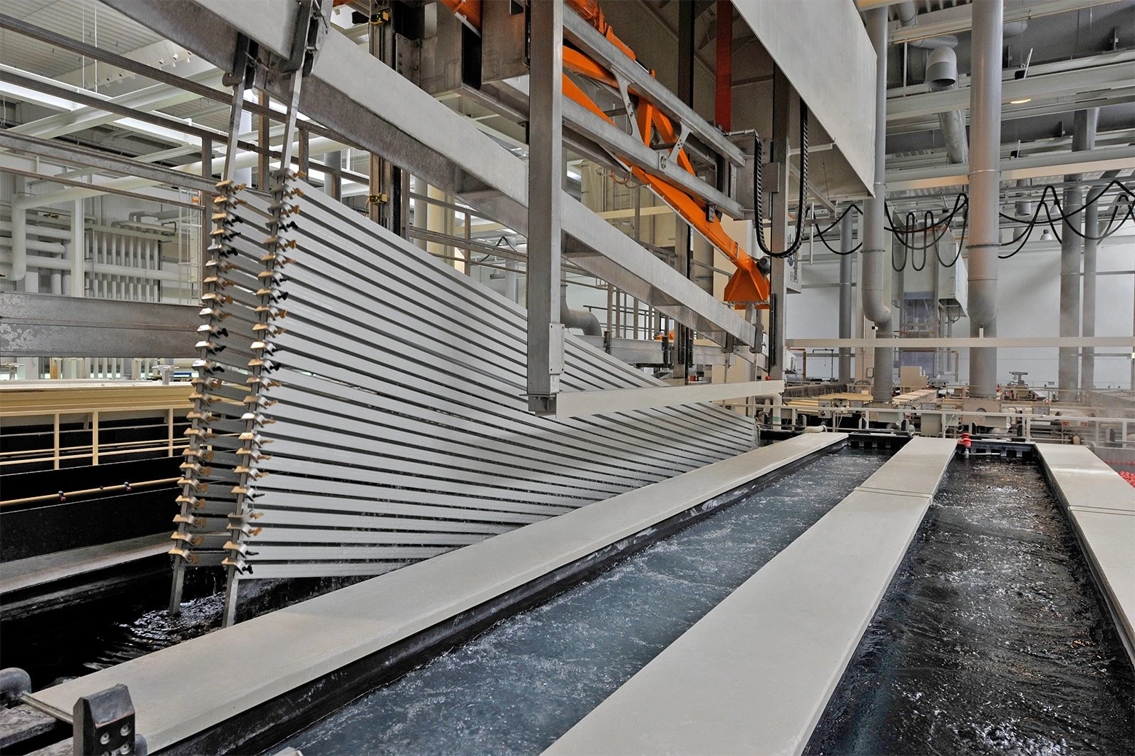 Aluminum parts being dipped into an electrolyte solution tank during the anodization treatment to form a hard oxide film substrate before painting.