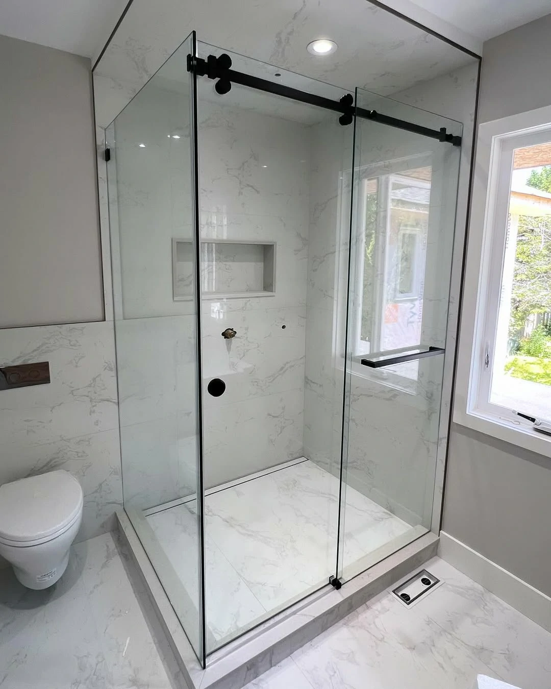 Frameless sliding shower door system with exposed matte black rollers and top track.